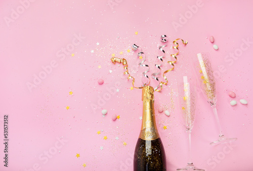 Champagne bottle with confetti on pink background.