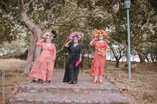 Group portrait of three women with the makeup of the catrinas.. Makeup for the celebration of Day of the Dead in Mexico. Outdoors portrait.