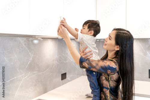 Mother choosing kitchen cabinet pull handle while caring for child son in arms. Representing mom life and a stay at home mom.