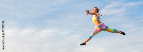 Young girl gymnast in bright tracksuit flies in long jump against background of blue summer evening sky. There is no ground under your feet.
