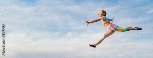 Young girl gymnast in bright tracksuit flies in long jump against background of blue summer evening sky. There is no ground under your feet.