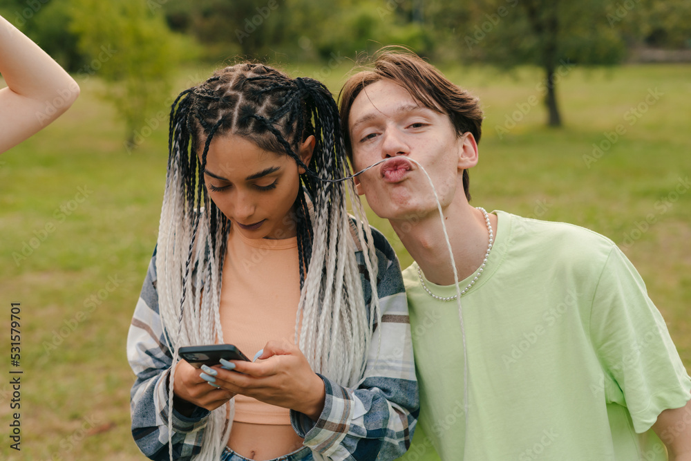 Boy playing with the girl's hair, who is looking at the phone, concentrating on typing messages. Outdoor lifestyle. Youth lifestyle. College life. City