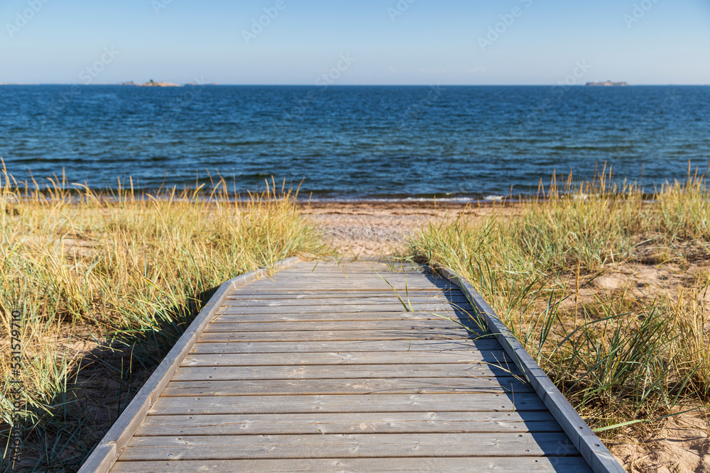 Obraz premium Wooden boardwalk leading to an empty beach in Hanko, Finland, on a sunny day in the summer. Focus on the front, shallow depth of field.