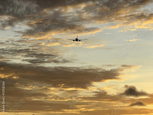 Airplane in the sky, flying into the distance in a golden sunset. Beautiful sundown. Plane in the skies, back view. Air transport. Amazing heaven with pattern of clouds. Sun glow. Twilight. Scenery 
