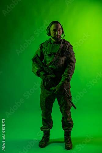 soldier in the studio on a green background with colored light. a man in military uniform with a gun, rifle or machine gun. military. airball player