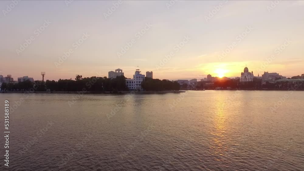 Aerial view of Sunrise in a big city on the river. The sun rises over the city. In the frame of the buildings and the church. The camera goes up
