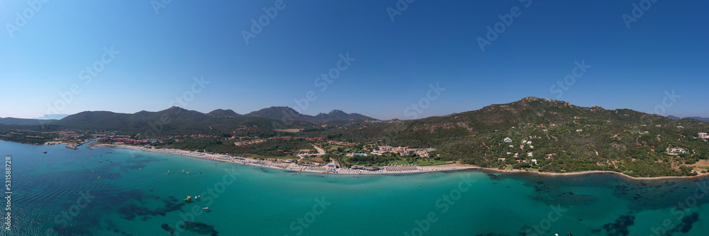 The beaches of Sardinia in the background mountains cumulus clouds top view. Sardinia panorama clear water aerial view. Sardinia famous beaches white sand clear turquoise water aerial view.