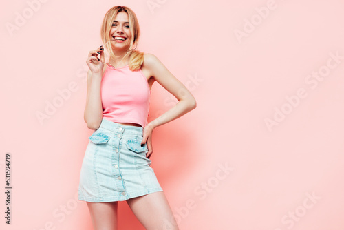 Young beautiful smiling blond female in trendy summer jeans skirt clothes. carefree woman posing near pink wall in studio. Positive model having fun indoors. Cheerful and happy