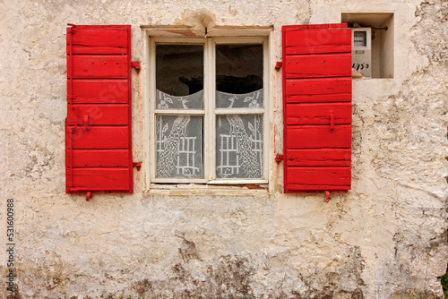 Picturesque facade of traditional local house with stone wall, red window and elaborate lace curtains, seen in a village of Zakynthos island, Greece
