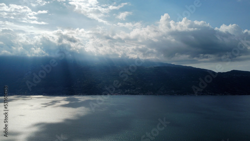 See mit bergiger Küste im Hintergrund und durchbrochener Wolkendecke