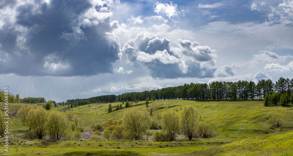 Spring landscape, dramatic sky over green hills before rain. The sun through the clouds illuminates the green meadows and ravines. Spring landscape, dramatic sky over green hills before rain. The sun through the clouds illuminates the green meadows and ravines.