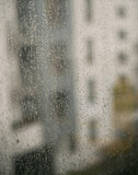 Raindrops on a window with an apartment house background. Concept of staying home while there is bad weather outside. Cozy indoor view at rainy weather