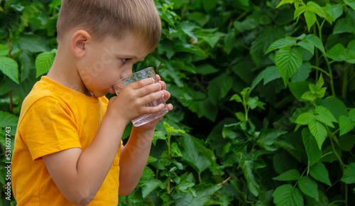 little boy drinking water with a glass in the park.