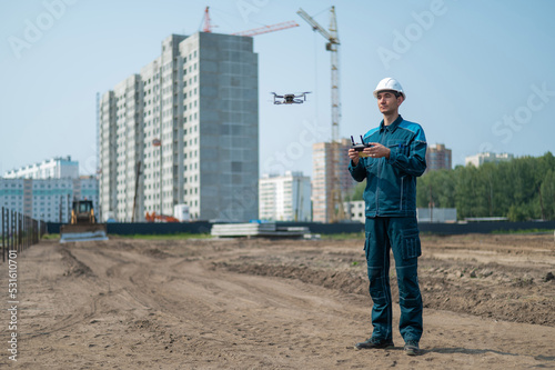 A man in a helmet and overalls controls a drone at a construction site. The builder carries out technical oversight. © Михаил Решетников