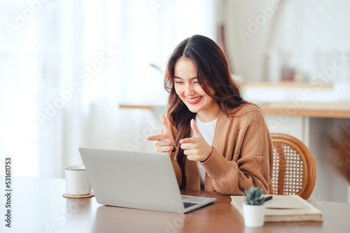 Happy positive young asian woman enjoying online communication at home  Female using wifi while video conferencing with friend  sitting in front of open laptop  copy space.
