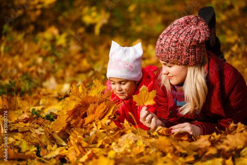 Mother and daughter having fun in the autumn park among the falling leaves.