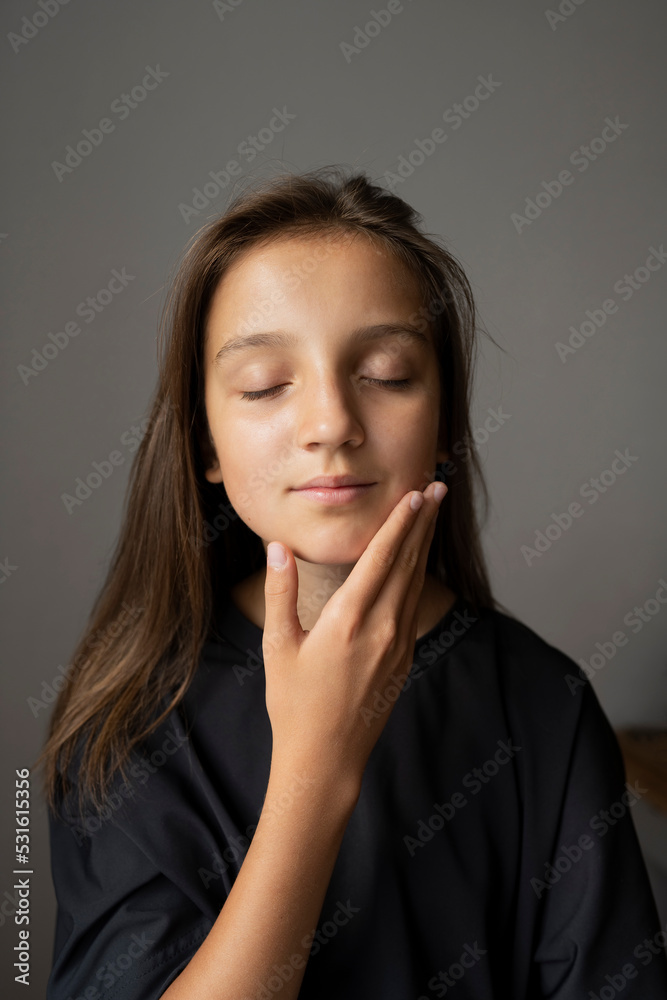 Girl with eyes closed touching face against gray wall Girl with eyes closed touching face against gray wall