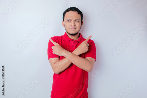 Portrait of a thoughtful young casual man wearing a red shirt pointing upside isolated over white background