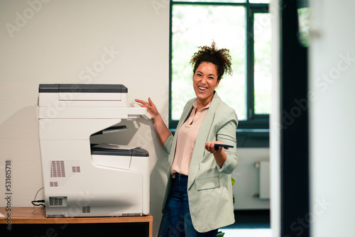 Cheerful businesswoman standing by computer printer at workplace photo