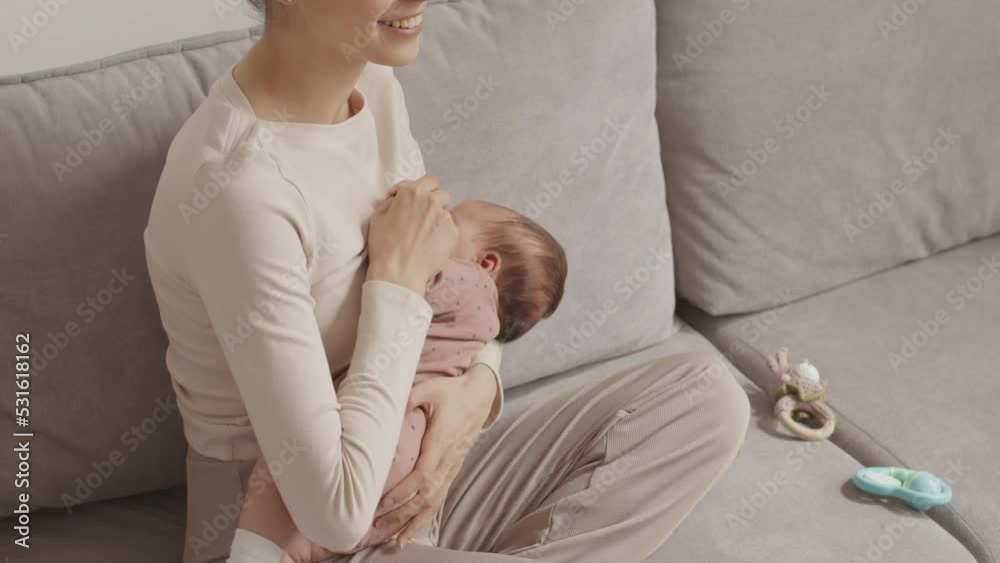 From above slowmo of young Caucasian woman with infant baby daughter in her arms sitting on sofa at cozy home From above slowmo of young Caucasian woman with infant baby daughter in her arms sitting on sofa at cozy home