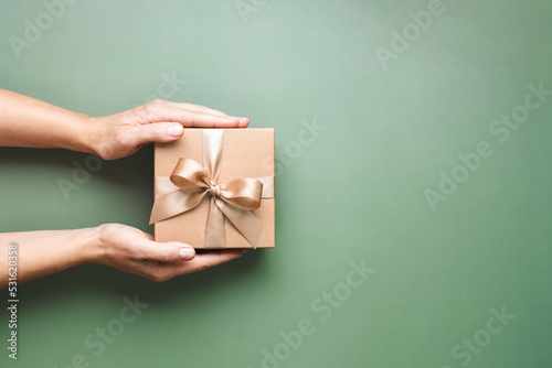 Female hands holding Christmas gift box on pastel green background. photo