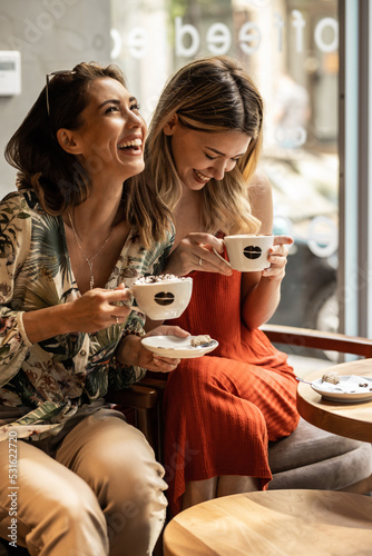 Beautiful happy women talking and laughing while drinking coffee together in coffee shop.