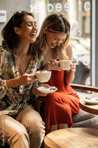 Beautiful happy women talking and laughing while drinking coffee together in coffee shop.