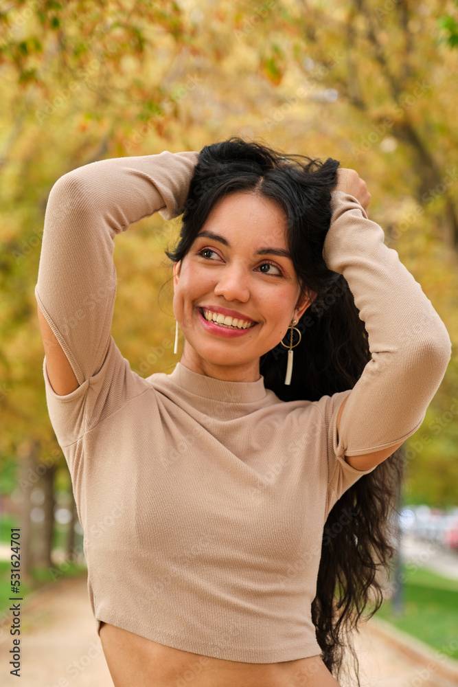 Young latin girl holding her hair and smiling at street in autumn. Young latin girl holding her hair and smiling at street in autumn.