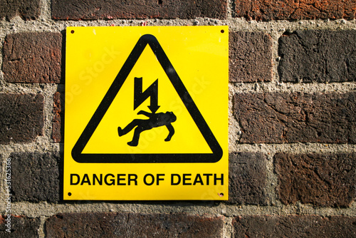 Photography A bright yellow sign that says danger of death with an image of a lighting bolt hitting someone in the chest