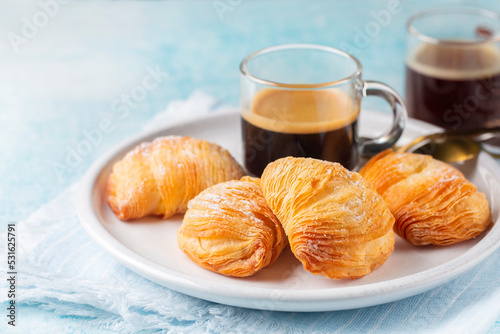 Italian breakfast with coffee. Caffè Espresso and neapolitan shell-shaped pastry sfogliatelle riccia stuffed with ricotta, almond paste and candied citron. Or lobster tail. Light blue background.