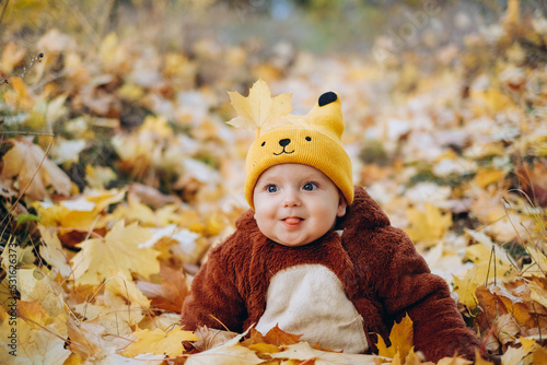 The kid sits in yellow leaves in the park for a walk.