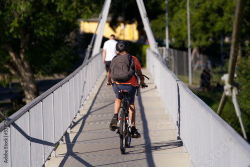 Pedestrian rope bridge with school kid on bicycle at village Kleinandelfingen, Canton Zürich, on a sunny summer morning. Photo taken July 12th, 2022, Kleinandelfingen, Switzerland. photo