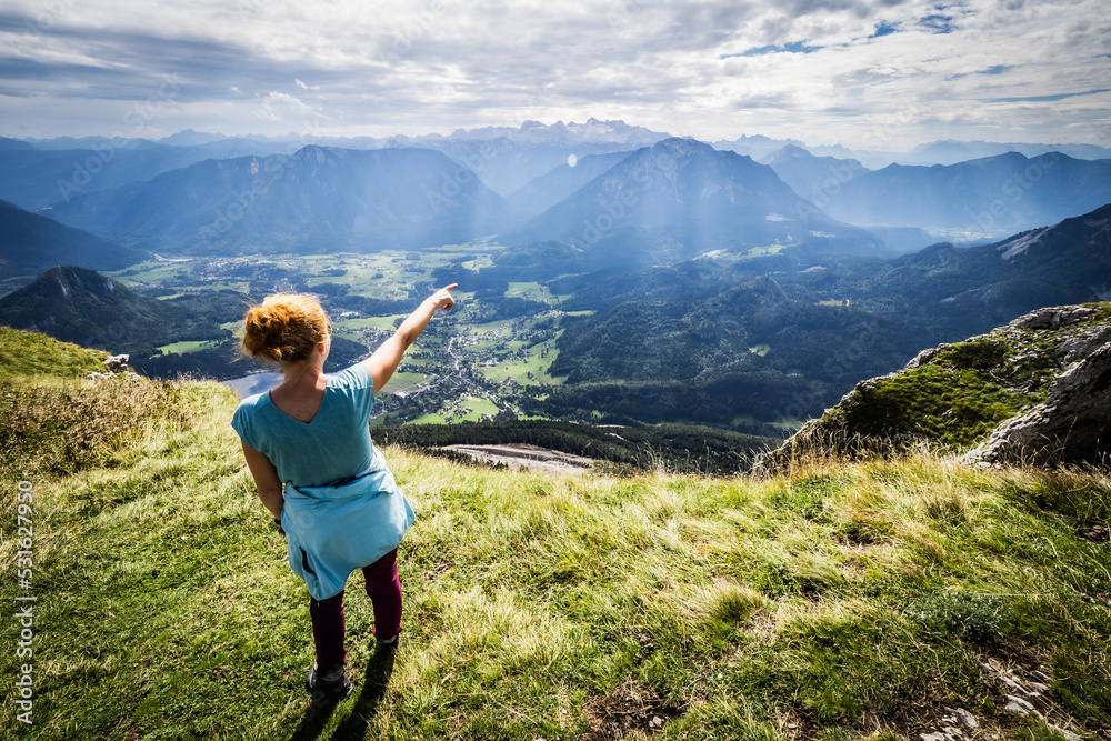 Female hiker enjoys the breathtaking view from the top of Loser mountain and points to the opposite peak, Altaussee, Ausser Land, Styria, Austria