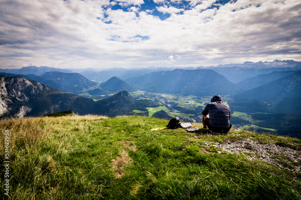 Male hiker sitting in grass and enjoys a breathtaking view from the summit of Loser mountain, Altaussee, Ausser Land, Salzkammergut, Styria, Austria