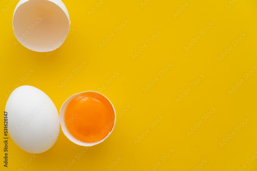 Top view of natural yolk in shell near white egg on yellow background.