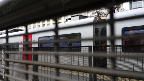 Panning shot of train leaving behind fence in station with second class carriages visible photo