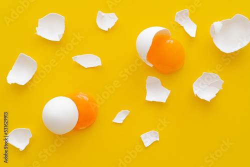 Top view of natural yolks and cracked egg shells on yellow background.