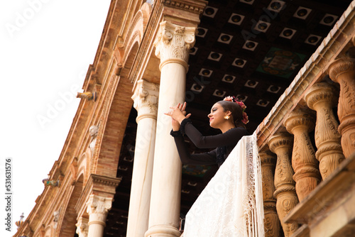 Foto A beautiful teenage flamenco dancer with brown hair stands on a balcony between two white marble columns and performs flamenco dance postures and claps her hands artfully