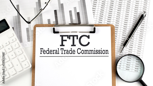 Paper with FTC -FEDERAL TRADE COMMISSION on a chart with calculator,pen and magnifier