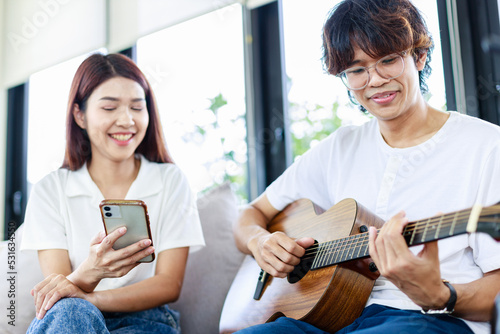 Happy couple at home, A Young man playing guitar to girlfriend in living room, Leisure activities