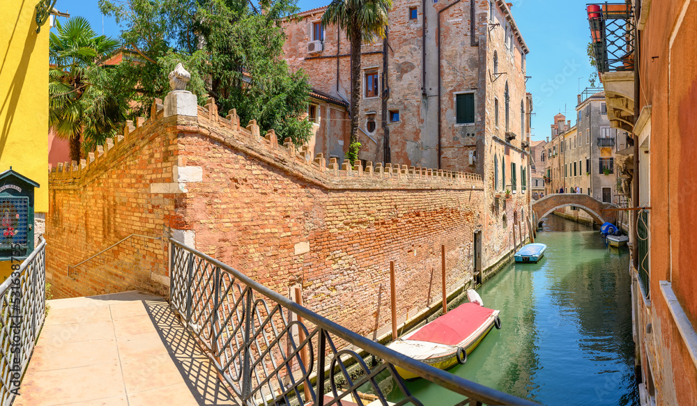 View on the narrow cozy streets of the canals with bridges and parked boats in Venice, Italy. Architecture and landmark of Venice.