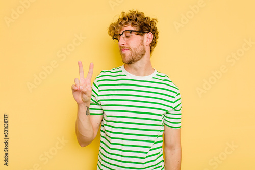 Young caucasian man isolated on yellow background joyful and carefree showing a peace symbol with fingers.
