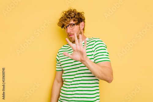 Young caucasian man isolated on yellow background being shocked due to an imminent danger