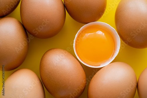 Close up view of fresh yolk in shell near eggs on yellow background.