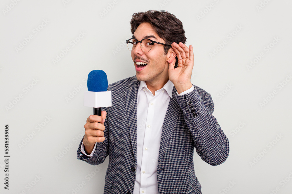 Young hispanic TV presenter man isolated on white background trying to listening a gossip. Young hispanic TV presenter man isolated on white background trying to listening a gossip.