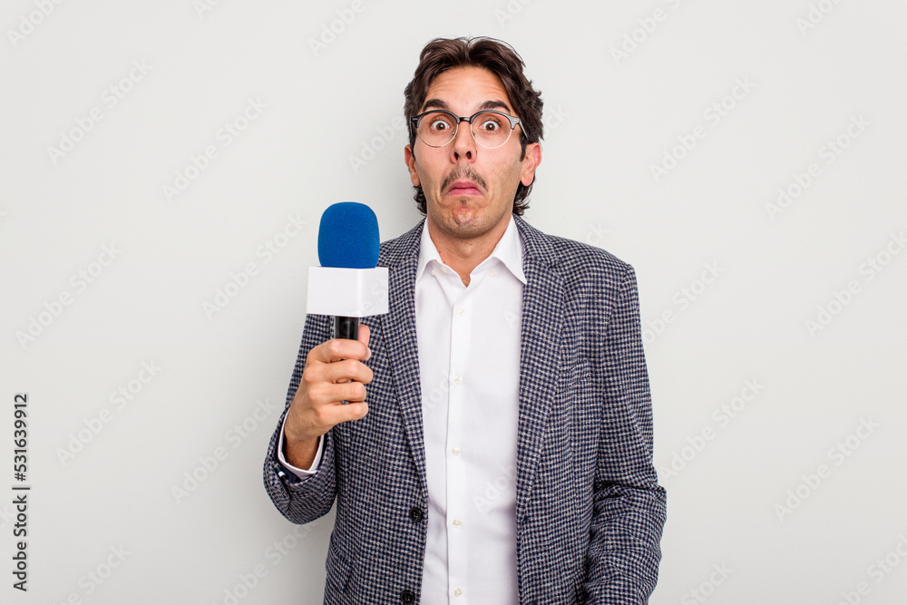 Naklejka premium Young hispanic TV presenter man isolated on white background shrugs shoulders and open eyes confused.