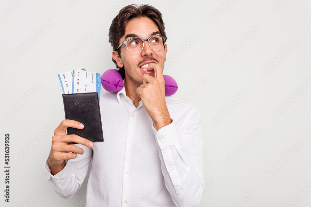 Young hispanic man with inflatable travel pillow holding passport isolated on white background relaxed thinking about something looking at a copy space. Young hispanic man with inflatable travel pillow holding passport isolated on white background relaxed thinking about something looking at a copy space.