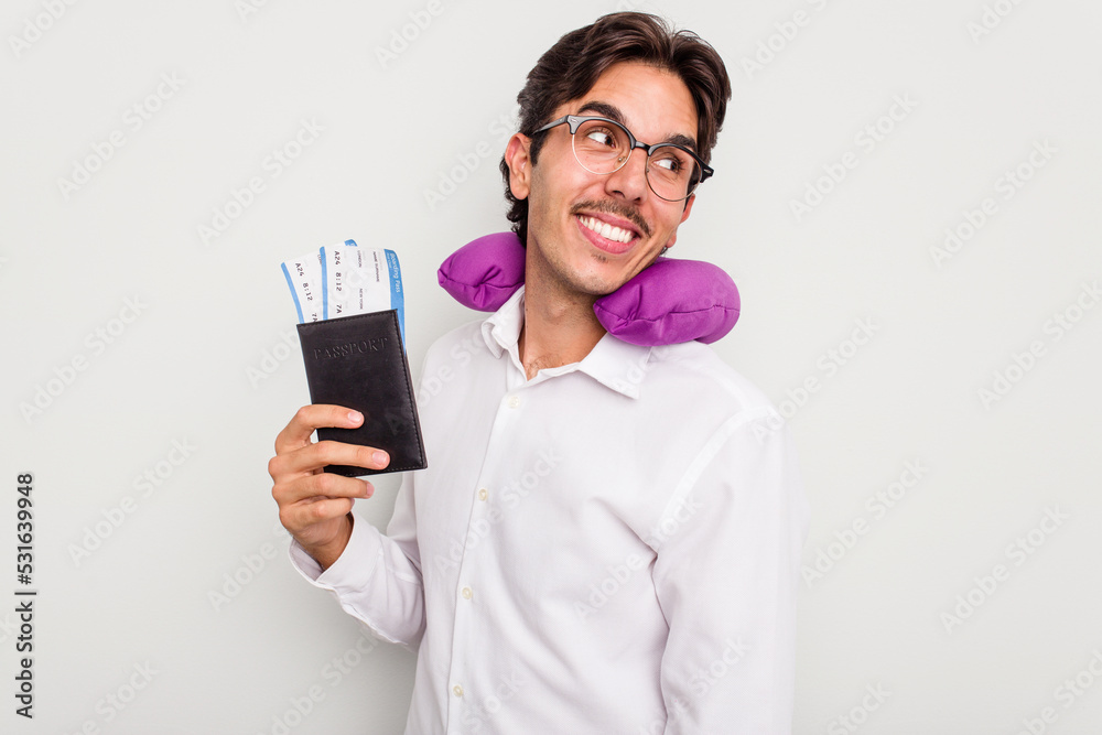 Young hispanic man with inflatable travel pillow holding passport isolated on white background looks aside smiling, cheerful and pleasant. Young hispanic man with inflatable travel pillow holding passport isolated on white background looks aside smiling, cheerful and pleasant.
