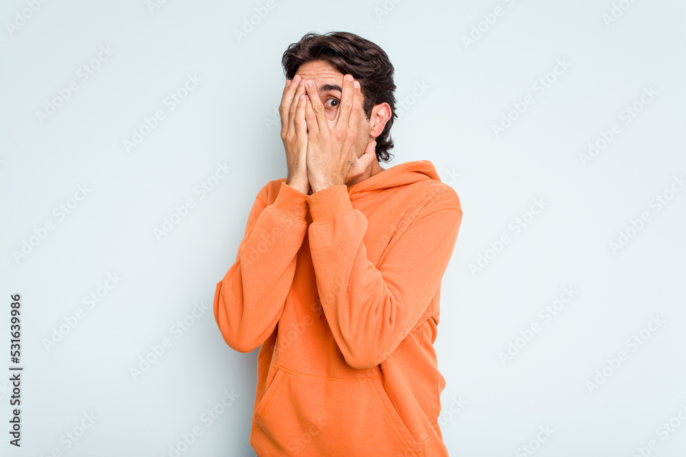 Young hispanic man isolated on blue background blink through fingers frightened and nervous. Young hispanic man isolated on blue background blink through fingers frightened and nervous.