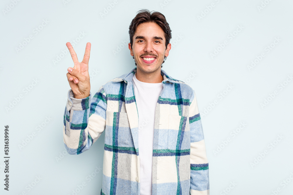 Young hispanic man isolated on blue background joyful and carefree showing a peace symbol with fingers. Young hispanic man isolated on blue background joyful and carefree showing a peace symbol with fingers.